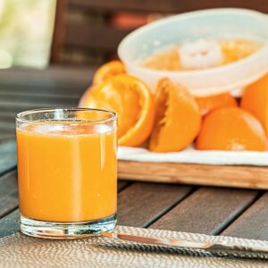 Glass of fresh orange juice with sliced oranges on wooden table, perfect for breakfast and healthy living.